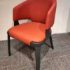 Red upholstered dining chair with curved backrest and black metal legs, angled front view from the Aurelia Series