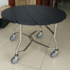 Round folding banquet table with matte black drop-leaf top, chrome legs, and caster wheels for hotel dining or catering use