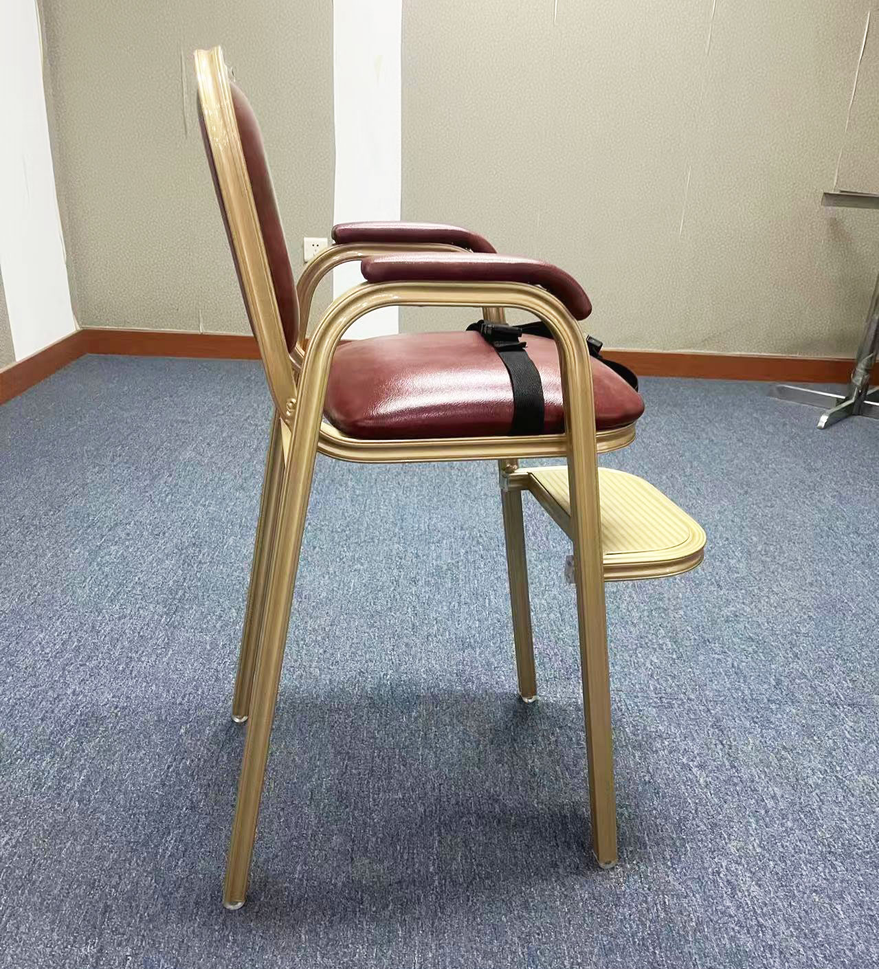 Side angle of maroon upholstered hotel baby high chair with armrests, footrest, and safety belt