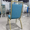 Angled rear view of Valenza banquet chair with blue upholstered backrest and gold powder-coated steel frame, in factory setting