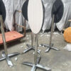 Foldable cocktail tables in vertical storage position with white woodgrain round tops and chrome X-bases, shown in a factory setting