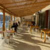 White metal dining chairs with wood seats arranged in a waterfront restaurant terrace with wood tables and harbor view