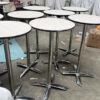Bulk view of foldable round cocktail tables with white woodgrain laminate tops and chrome bases, assembled in workshop