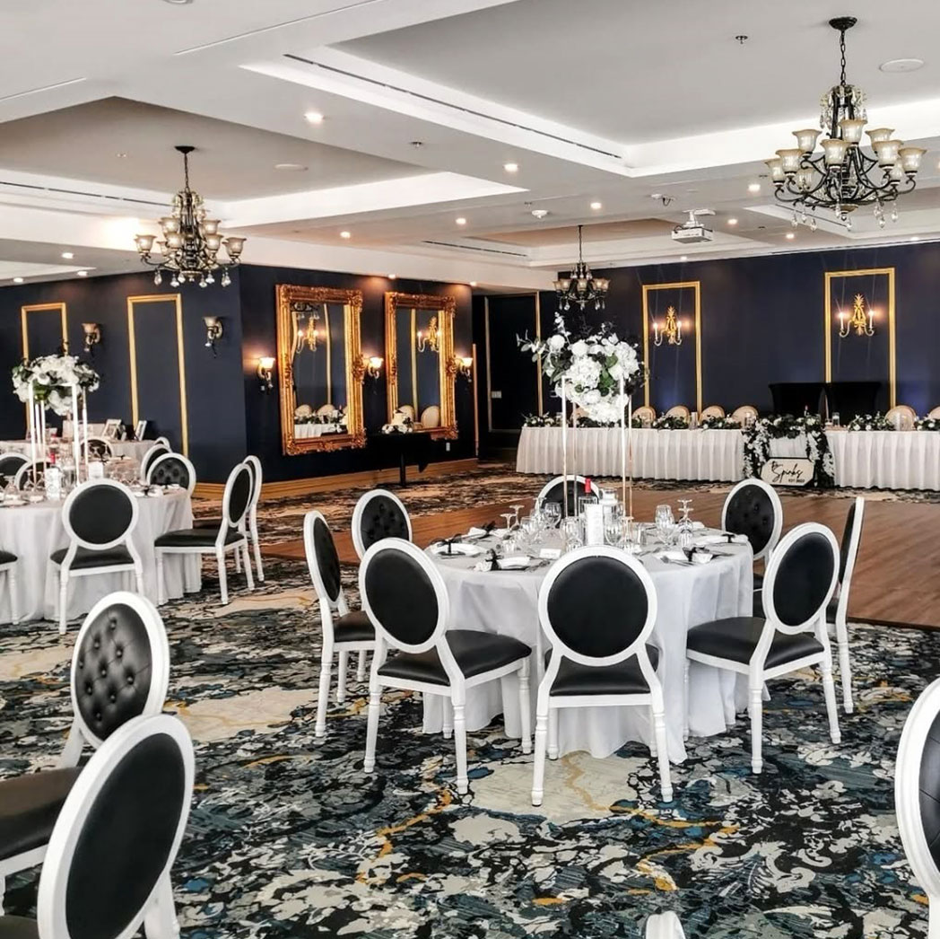 Elegant hotel banquet hall featuring white frame Louis-style chairs with black upholstered seats and tufted backs, arranged around round dining tables