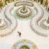 Aerial view of outdoor wedding reception featuring white serpentine banquet tables arranged in flowing curves around a central floral round table
