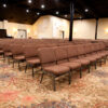 rows of upholstered aluminum church chairs in brown fabric arranged in a conference hall seating layout for church and event use
